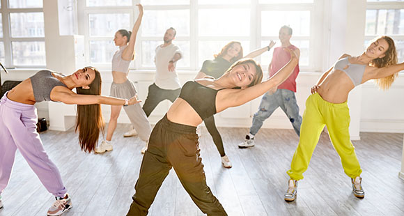 a group of people doing a stretch dance fitness move in a sunny dance studio